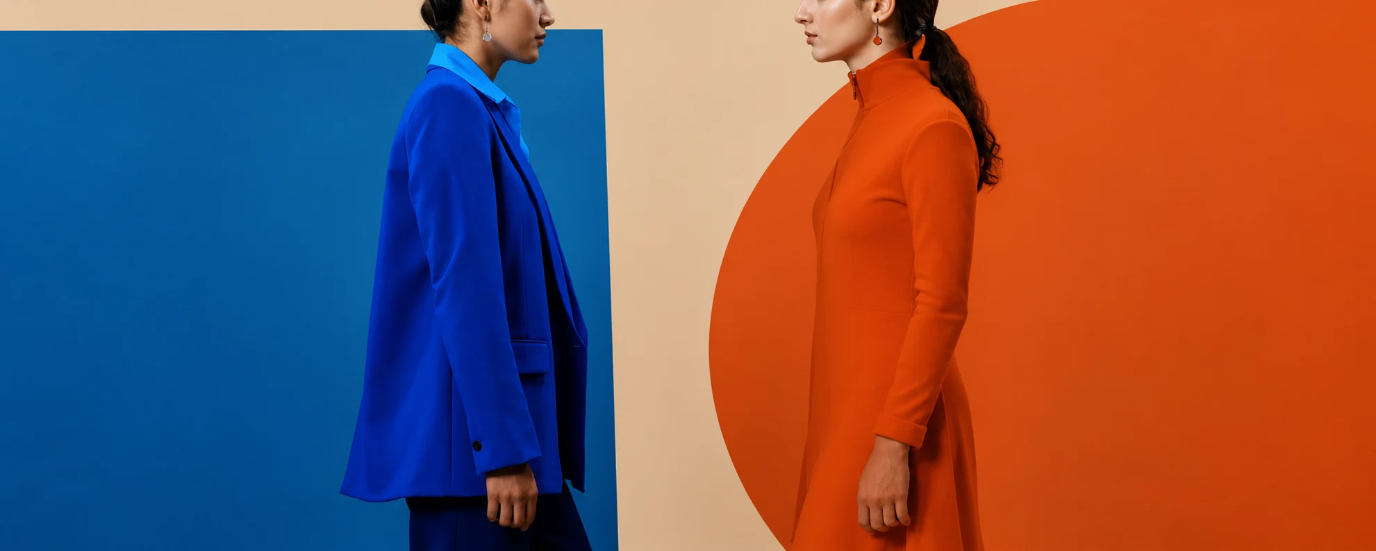 Two women in cobalt blue and burnt orange suits facing one another against a color-blocked background